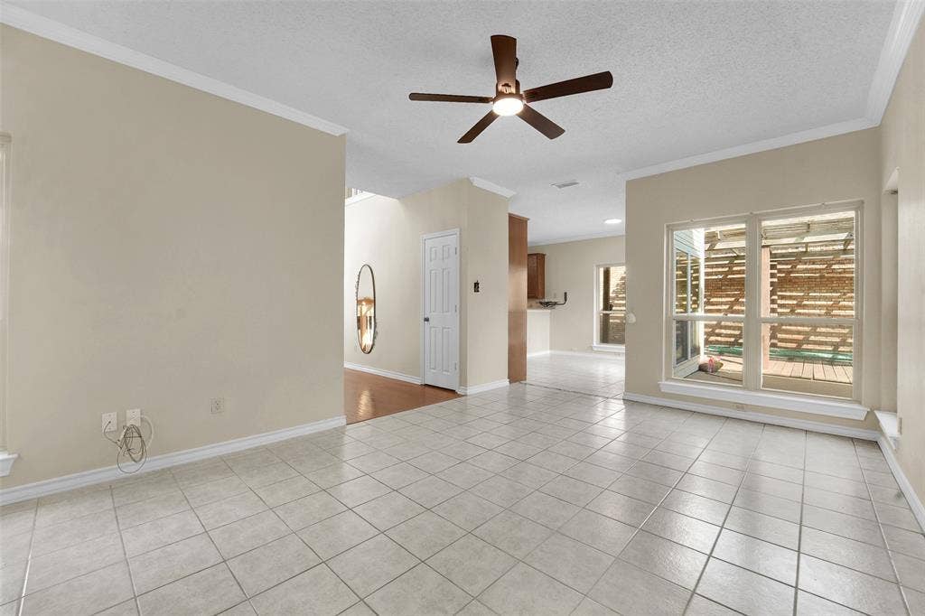 1920 Keystone Drive, Plano, TX 75075 Neutral-toned interior featuring ceramic tile flooring, a central ceiling fan with integrated lighting, expansive window sets, crown molding, and a multi-panel interior door