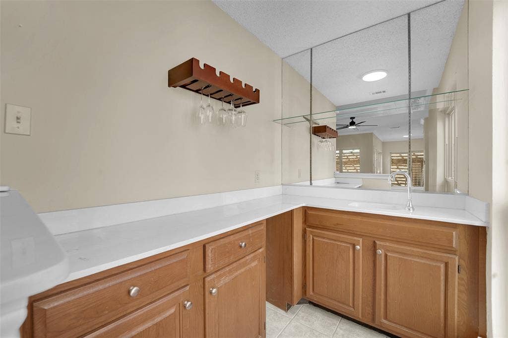 1920 Keystone Drive, Plano, TX 75075 Wet bar featuring wood-finish cabinetry, solid-surface countertops, a stainless steel gooseneck faucet, integrated sink, and full-height mirrored backsplash