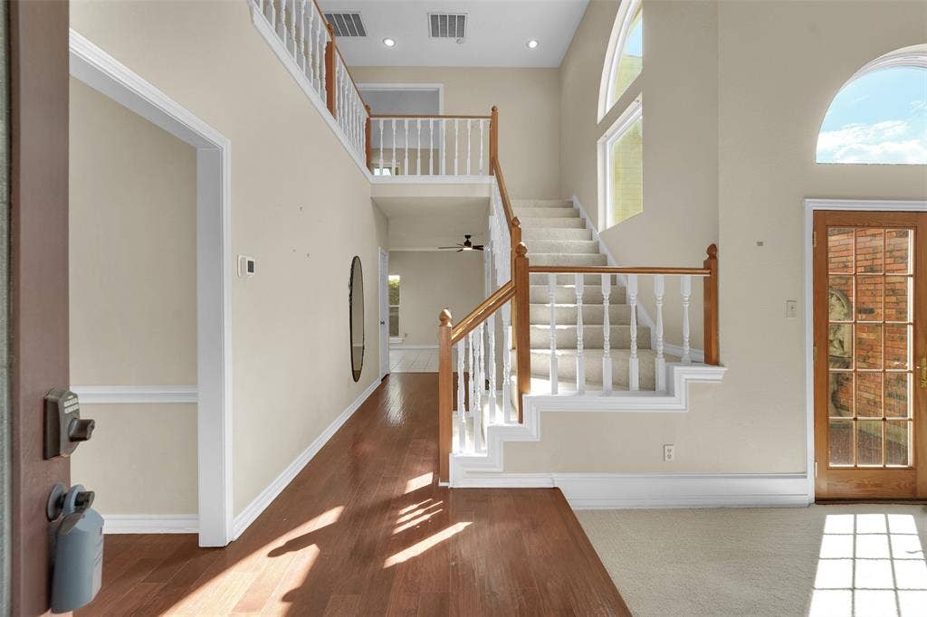 1920 Keystone Drive, Plano, TX 75075 Foyer featuring high ceilings, hardwood flooring, a staircase with a white balustrade and wood handrail, and arched windows