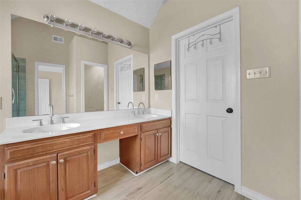 1920 Keystone Drive, Plano, TX 75075 Dual-sink vanity with wood-finish cabinetry, solid surface countertop, wall-to-wall mirror, and overhead light fixture