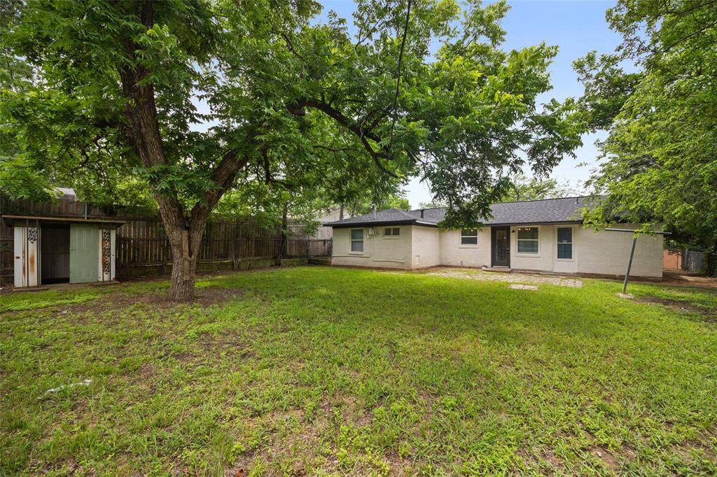 1605 Proctor Drive, Grand Prairie, TX 75051 Spacious backyard featuring a large mature tree, green lawn space, and a wood privacy fence