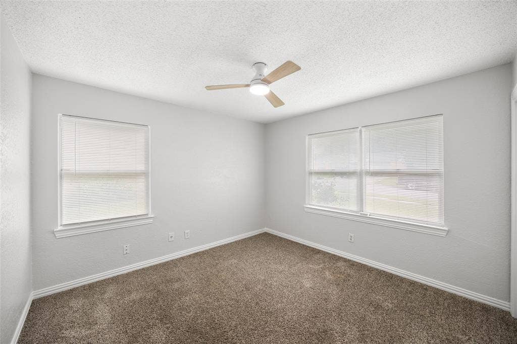 1605 Proctor Drive, Grand Prairie, TX 75051 Carpeted room featuring multiple windows with blinds, a ceiling fan with light fixture, and textured walls with baseboards