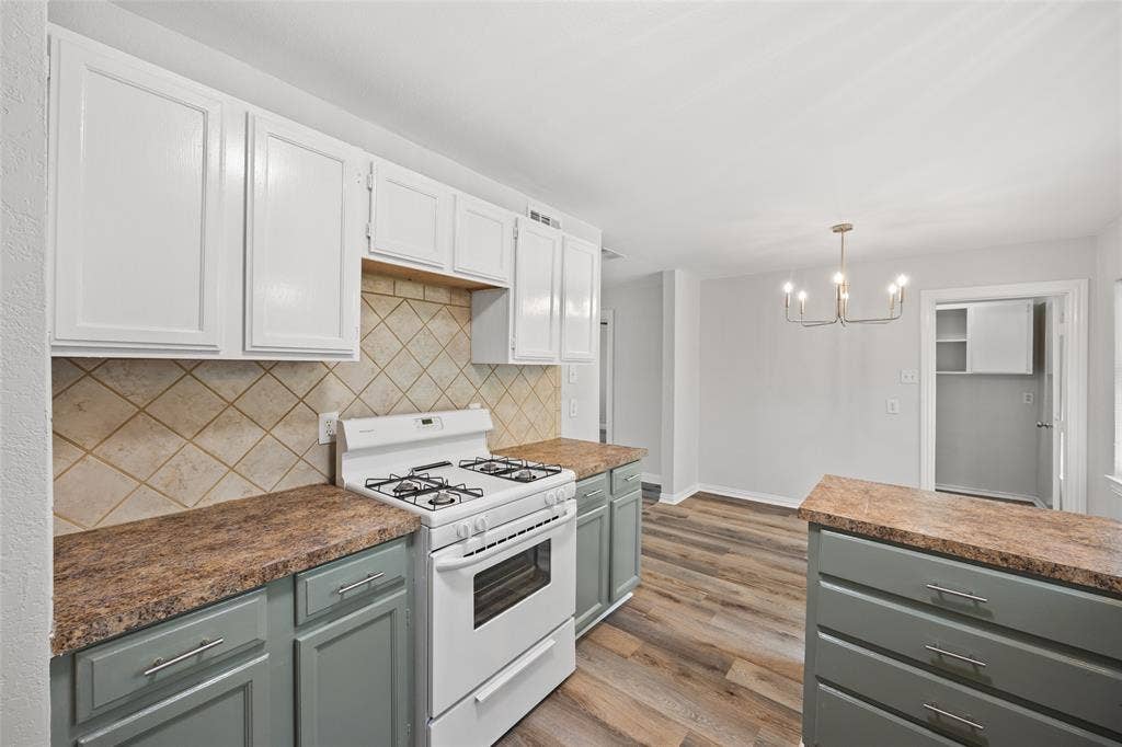 1605 Proctor Drive, Grand Prairie, TX 75051 Kitchen featuring two-tone cabinetry with white upper cabinets and gray lower cabinets, a gas range, diamond-patterned tile backsplash, and wood-finish flooring