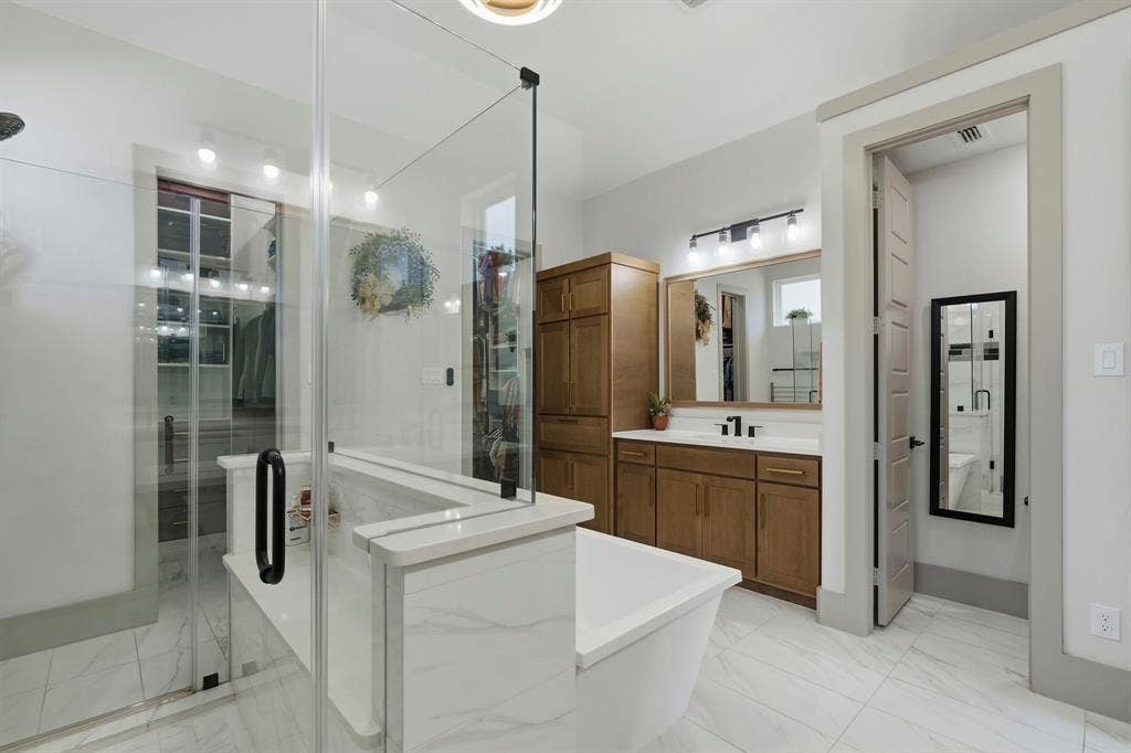 12173 Deer Trail, Frisco, TX 75035 Bathroom featuring large-format tile flooring, a glass-enclosed shower, a soaking tub with stone-finish surround, built-in wooden cabinetry, and a vanity with a rectangular sink and matching hardware