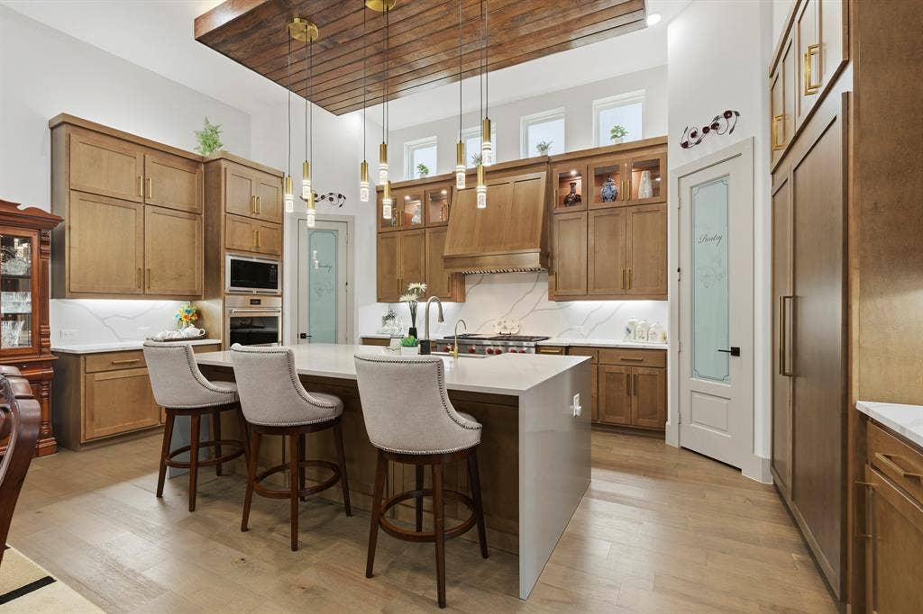 12173 Deer Trail, Frisco, TX 75035 Kitchen featuring floor-to-ceiling wood cabinetry, a center island with a waterfall countertop, suspended pendant lighting, wood-finish flooring, and a recessed ceiling panel with wood cladding