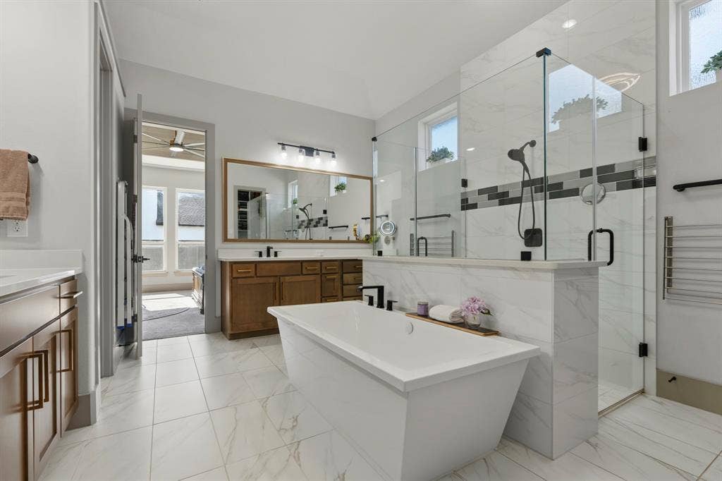 12173 Deer Trail, Frisco, TX 75035 Freestanding soaking tub, walk-in glass-enclosed shower with tile surround, wood-finish cabinetry, tile flooring, and wall-mounted vanity lighting