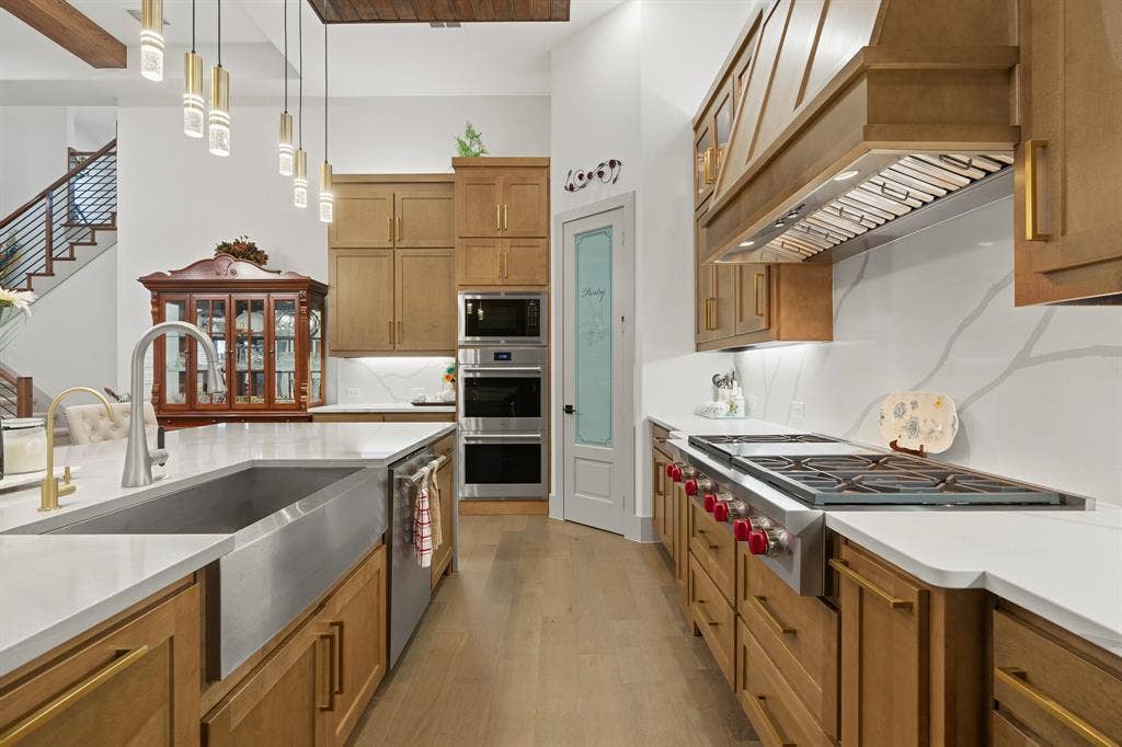12173 Deer Trail, Frisco, TX 75035 Gourmet kitchen featuring custom wood cabinetry, quartz countertops, stainless steel farmhouse sink, professional-grade gas range with integrated vent hood, and multi-light pendant fixtures