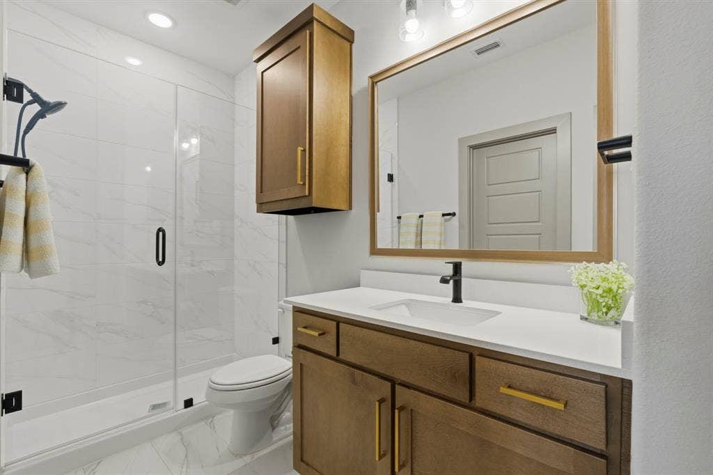 12173 Deer Trail, Frisco, TX 75035 Bathroom featuring wood-finish cabinetry with brass hardware, quartz countertop with integrated sink, walk-in shower with glass enclosure, and large-format tile flooring