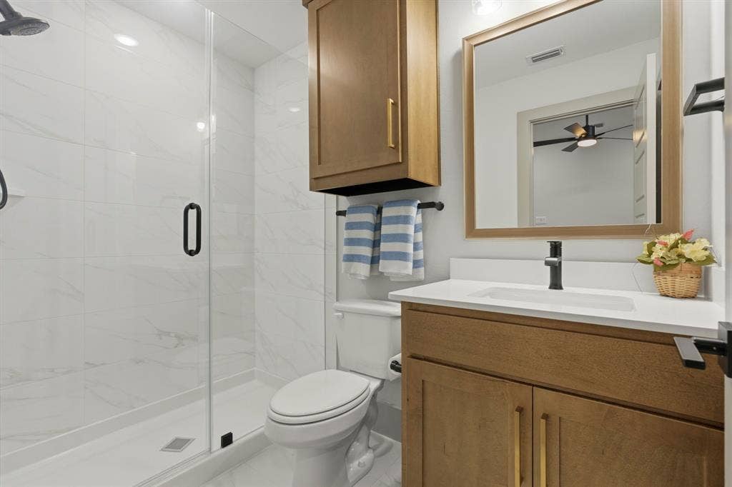 12173 Deer Trail, Frisco, TX 75035 Bathroom featuring a walk-in shower with glass enclosure, white stone-finish wall tile, wood-finish cabinetry, quartz countertop, and framed mirror
