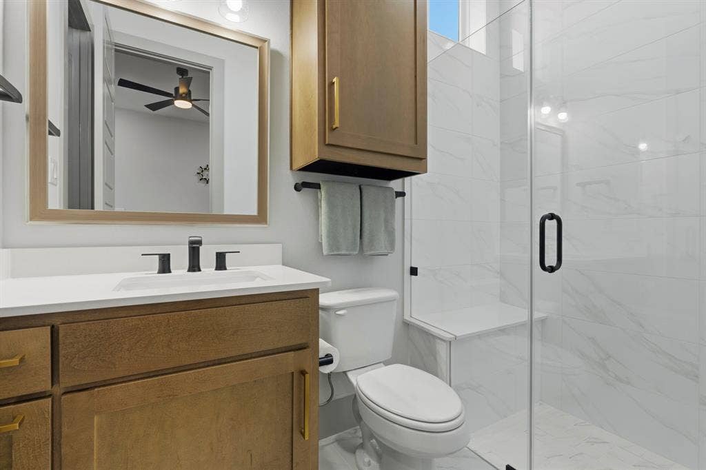 12173 Deer Trail, Frisco, TX 75035 Bathroom featuring a wood-finish vanity with a white countertop, wall-mounted cabinetry, a glass-enclosed shower with tiled walls and a built-in bench, and matte black fixtures