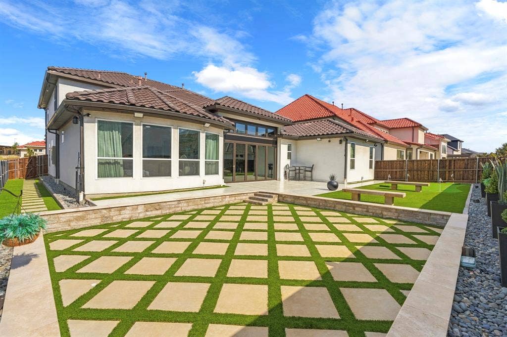 12173 Deer Trail, Frisco, TX 75035 Rear exterior featuring a multi-level terrace with geometric stone pavers and synthetic turf inlay, retaining walls, covered patio, and tile roof