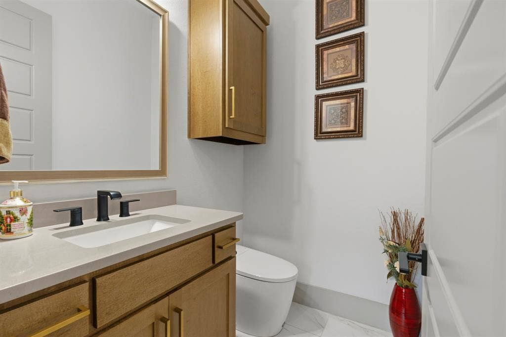 12173 Deer Trail, Frisco, TX 75035 Wood-finish vanity cabinet with a stone-composite countertop, rectangular undermount sink, matte black widespread faucet, and wall-mounted storage cabinet