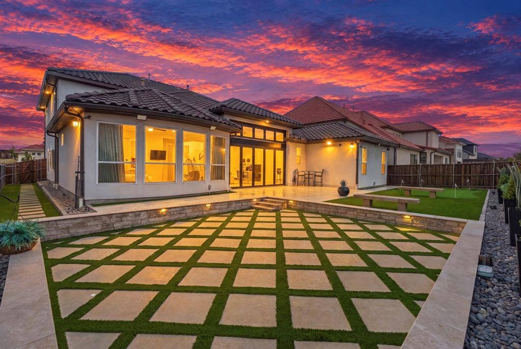 12173 Deer Trail, Frisco, TX 75035 Rear exterior featuring a tile roof, geometric paver patio with turf inlays, raised stone retaining walls with integrated landscape lighting, and a synthetic turf lawn