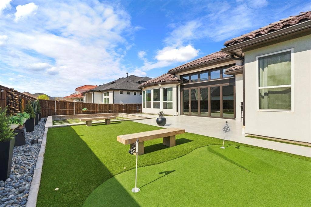 12173 Deer Trail, Frisco, TX 75035 Backyard featuring a synthetic grass putting green, concrete patio, tile roof, multi-panel sliding glass doors, and perimeter wood fencing