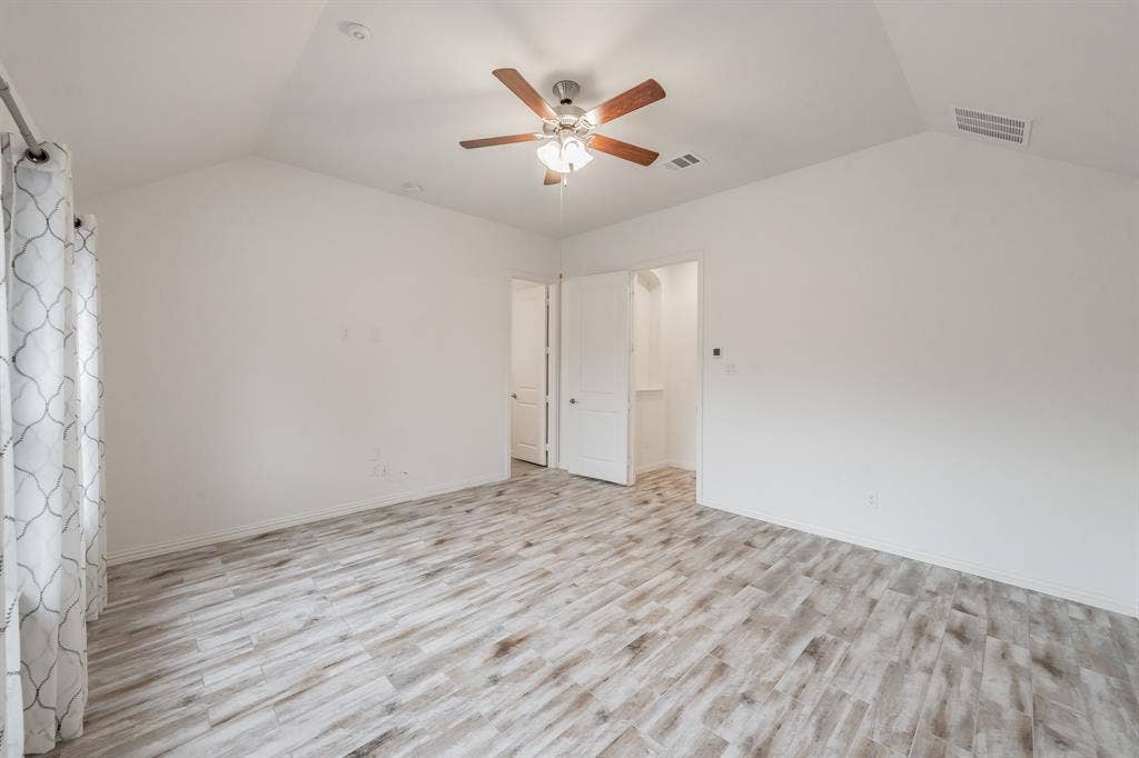 Spare room featuring vaulted ceiling, a ceiling fan, light wood-style floors, and baseboards