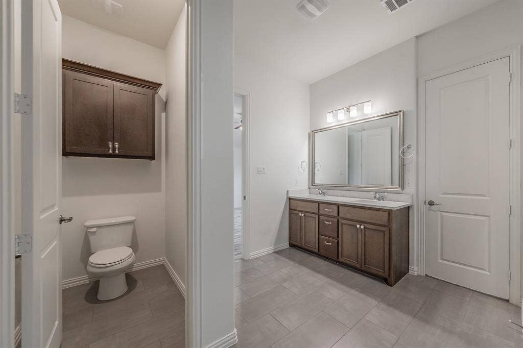 Full bath featuring double vanity, toilet, tile patterned floors, and baseboards