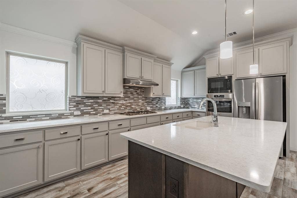 Kitchen with appliances with stainless steel finishes, light wood finished floors, gray cabinets, a sink, and vaulted ceiling