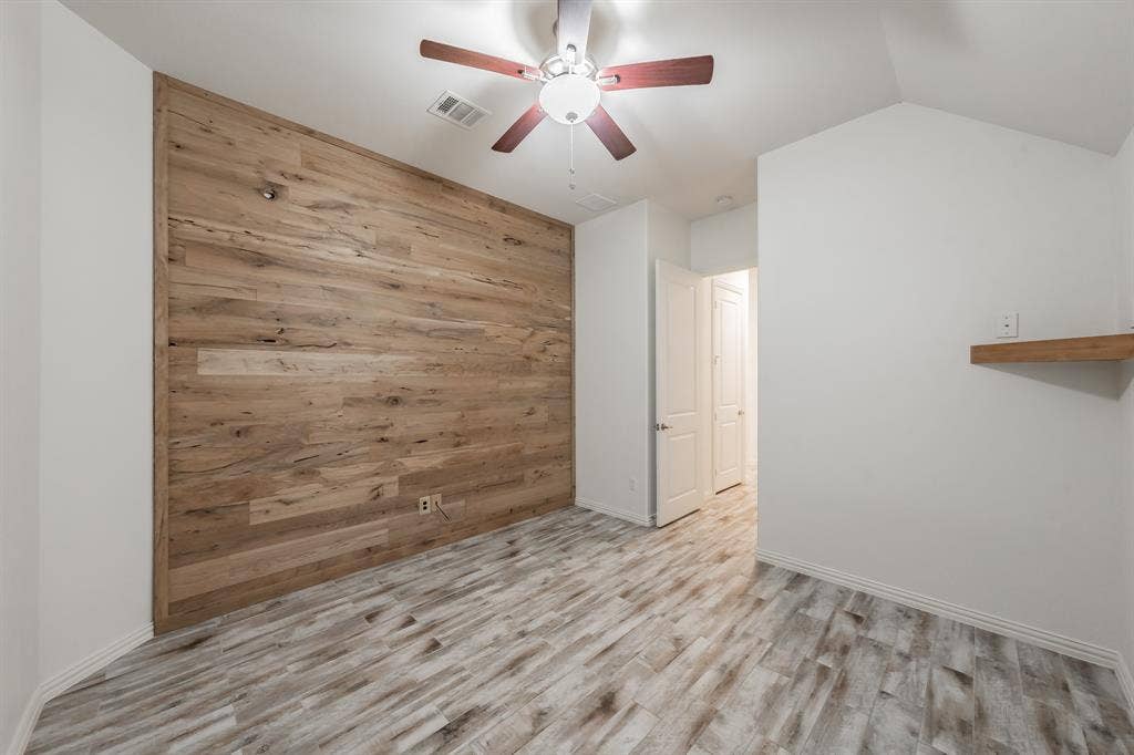 Spare room featuring wood walls, ceiling fan, wood finished floors, baseboards, and vaulted ceiling