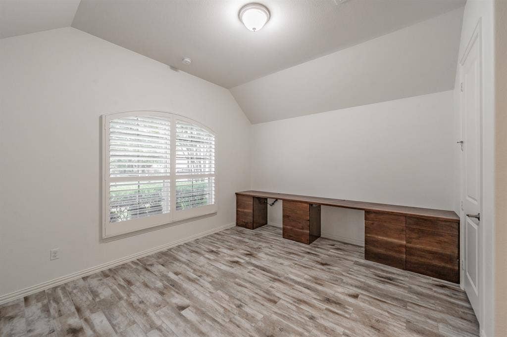 Unfurnished office with lofted ceiling, wood finished floors, and built in desk