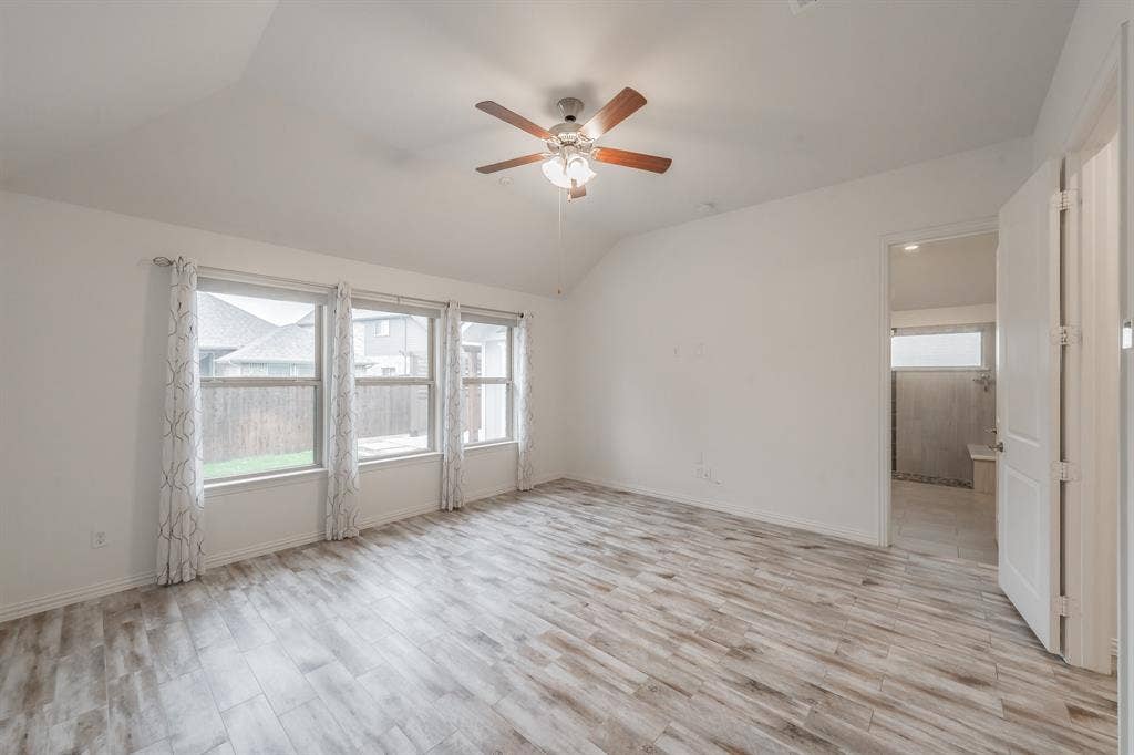 Unfurnished room featuring lofted ceiling, a ceiling fan, light wood-style floors, and baseboards