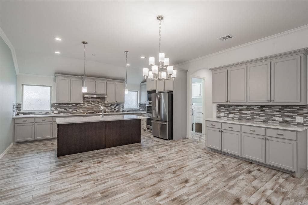Kitchen with gray cabinetry, appliances with stainless steel finishes, ornamental molding, backsplash, and light countertops