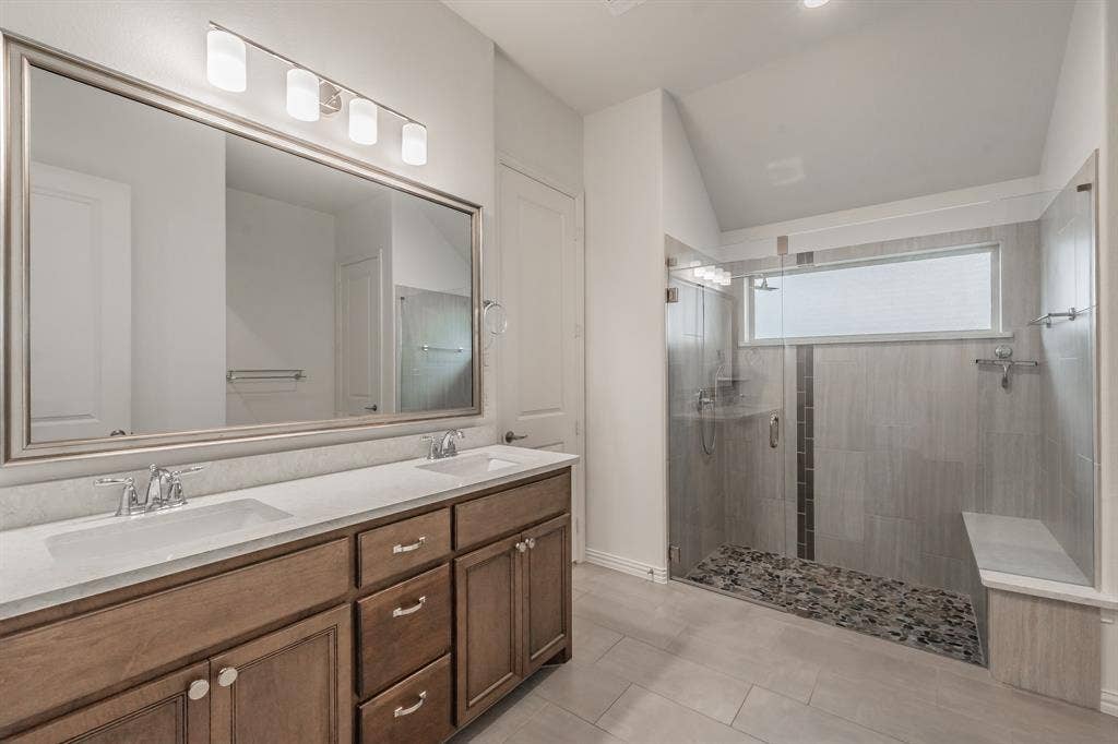 Bathroom featuring a stall shower, double vanity, tile patterned flooring, and vaulted ceiling