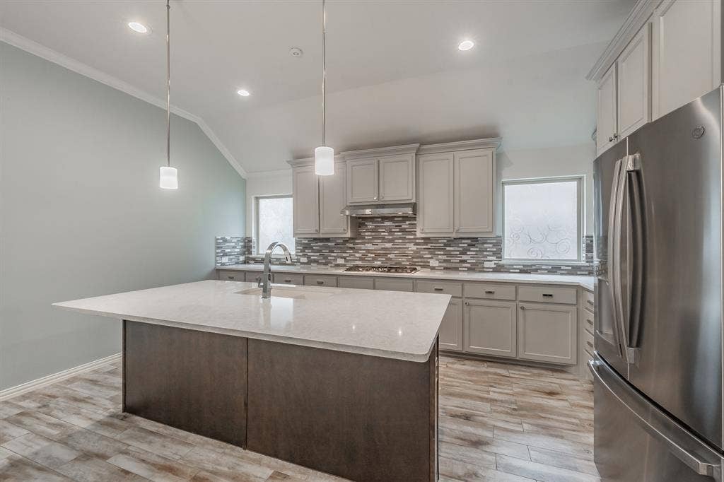 Kitchen featuring stainless steel appliances, a sink, ornamental molding, under cabinet range hood, and decorative backsplash