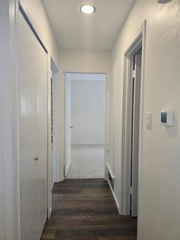Hallway featuring wood-finish flooring, recessed ceiling lighting, a built-in closet with double-panel doors, and a wall-mounted thermostat