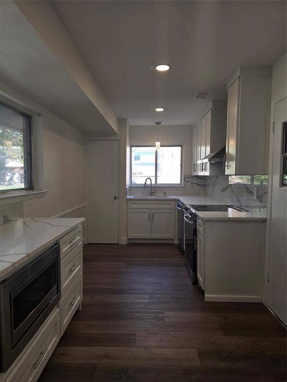 Kitchen featuring white shaker-style cabinetry, stone-patterned countertops, a full-height backsplash, stainless steel appliances, and dark wood-finish flooring