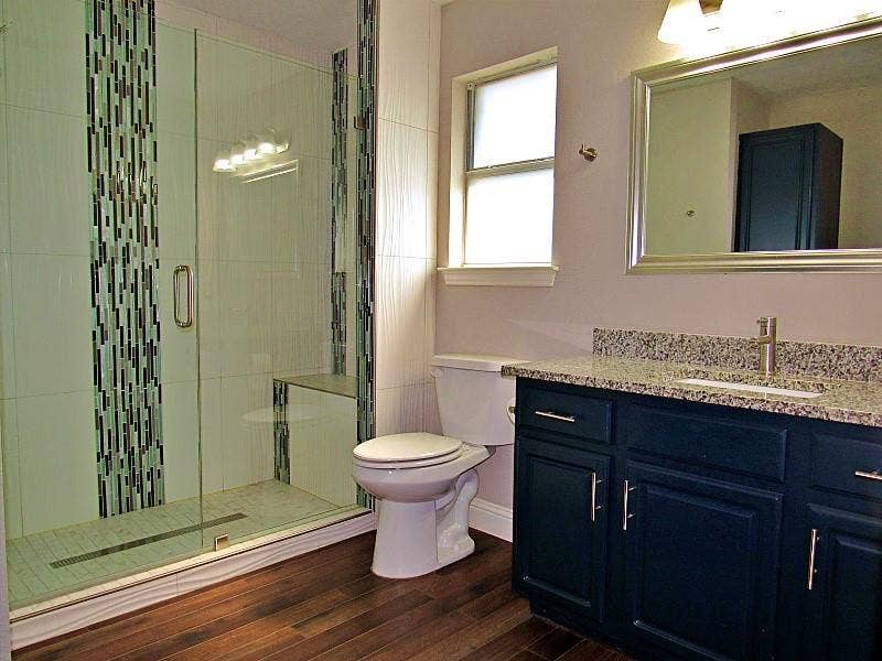313 Timbercreek Court, Princeton, TX 75407 Walk-in shower with vertical mosaic tile accents and glass door, navy blue vanity cabinet, stone-finish countertop, and wood-finish flooring