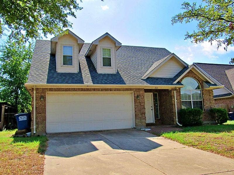 313 Timbercreek Court, Princeton, TX 75407 Brick exterior featuring dual front-facing dormer windows, a two-car garage, and an arched transom window