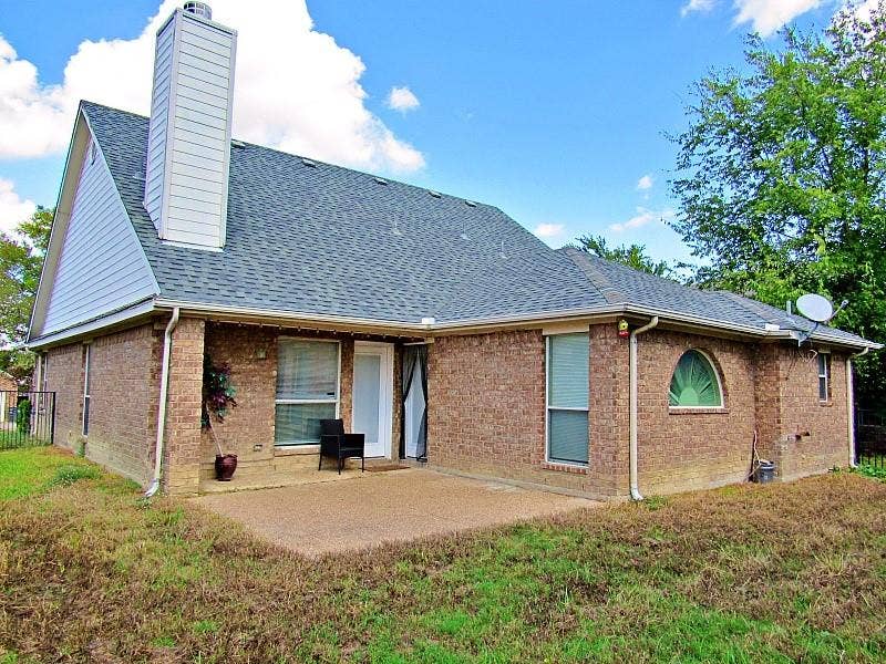 313 Timbercreek Court, Princeton, TX 75407 Brick exterior featuring a concrete patio, a tall chimney, and a decorative arched window