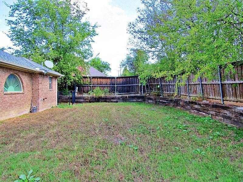 313 Timbercreek Court, Princeton, TX 75407 Backyard featuring a brick exterior wall, arched window, wood-paneled privacy fencing, and tiered landscape retaining walls