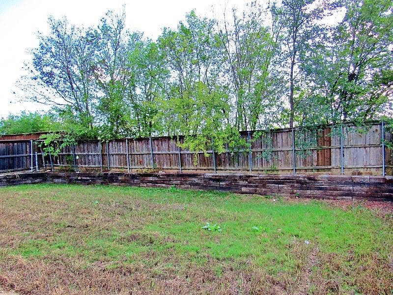 313 Timbercreek Court, Princeton, TX 75407 Backyard featuring a tiered timber retaining wall, vertical wood fencing, and mature trees