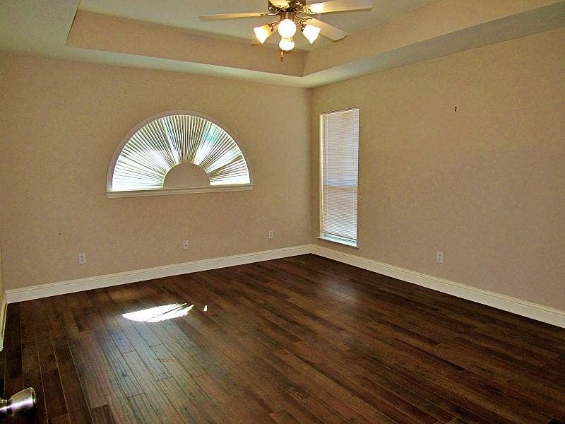313 Timbercreek Court, Princeton, TX 75407 Tray ceiling with a central multi-light fan, wood-finish flooring, and a decorative arched window