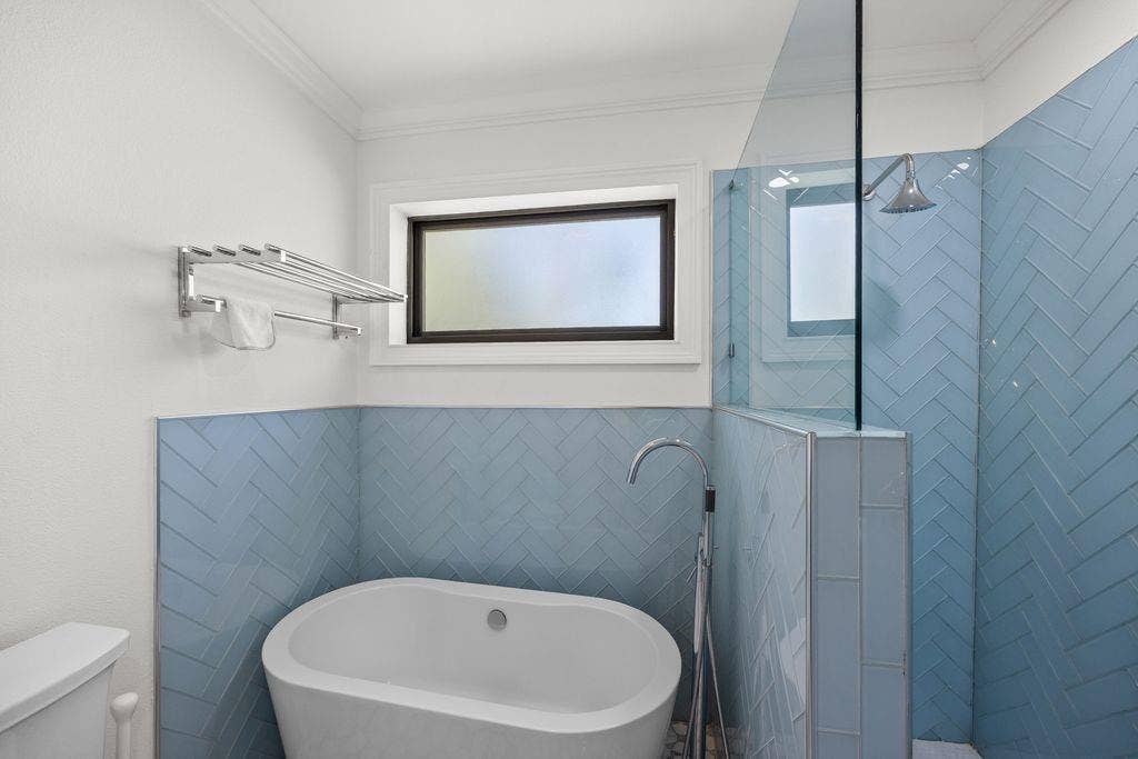 Freestanding soaking tub with a floor-mounted faucet, frameless glass shower enclosure, blue herringbone wall tile, and built-in wall-mounted towel rack