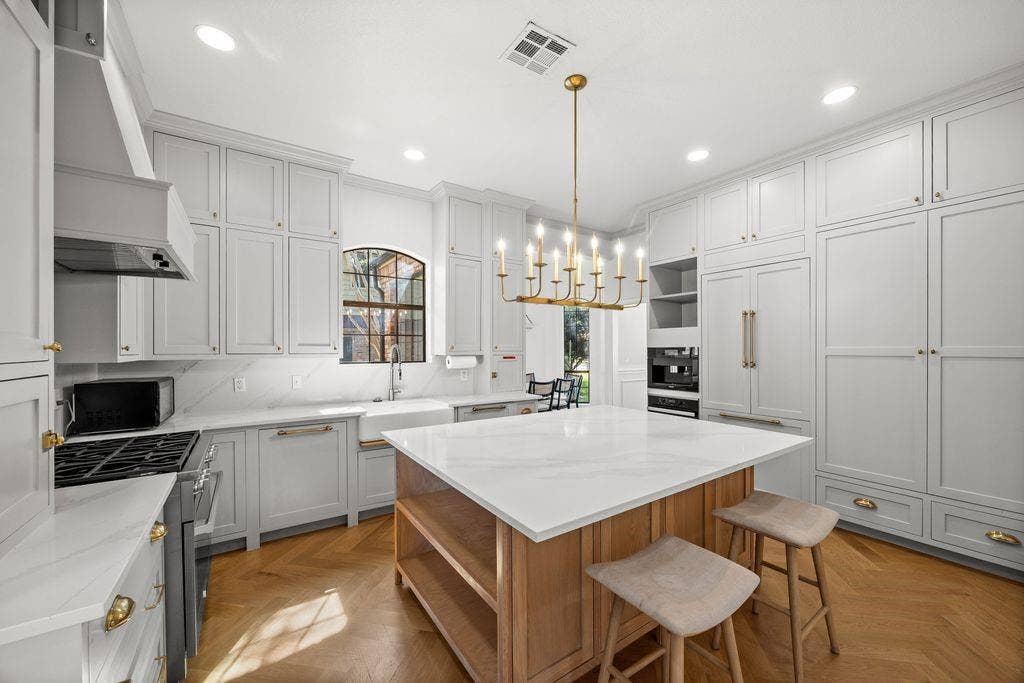 Kitchen featuring custom cabinetry, a central island with a stone countertop, herringbone wood-finish flooring, a farmhouse-style apron sink, and a multi-arm chandelier