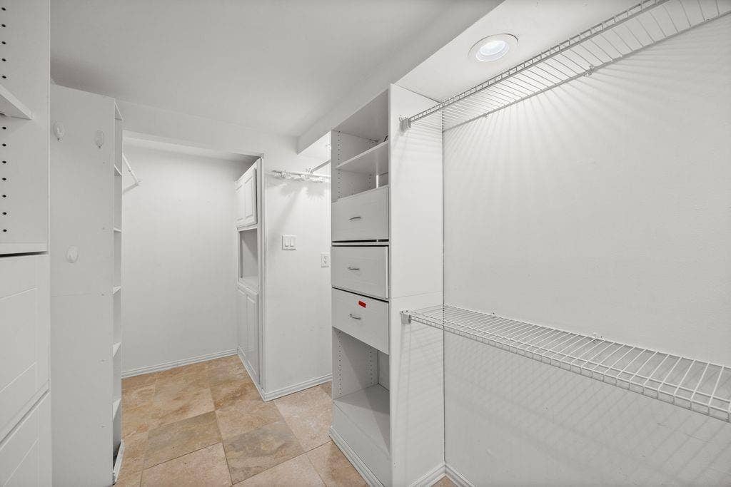 Custom walk-in closet featuring white built-in cabinetry, integrated drawers, wire shelving, and stone-finish flooring with recessed lighting