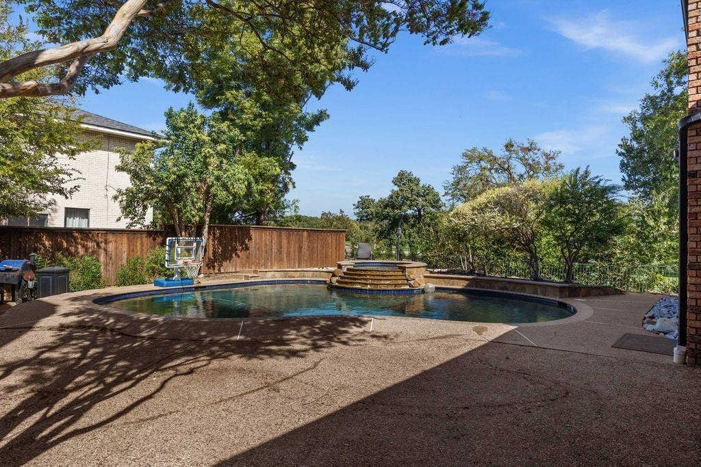 Backyard featuring a custom-shaped swimming pool, an integrated spa with cascading water, stamped concrete patio, and perimeter wood privacy fencing
