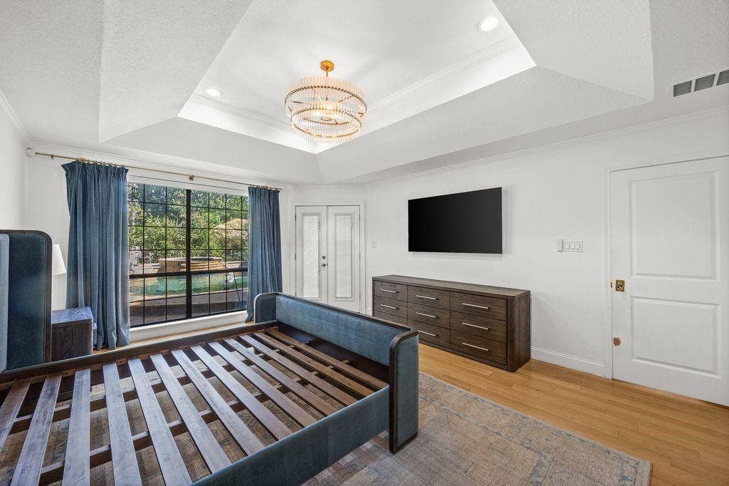Tray ceiling featuring a tiered chandelier and recessed lighting, large window with grid panes, and wood-finish flooring