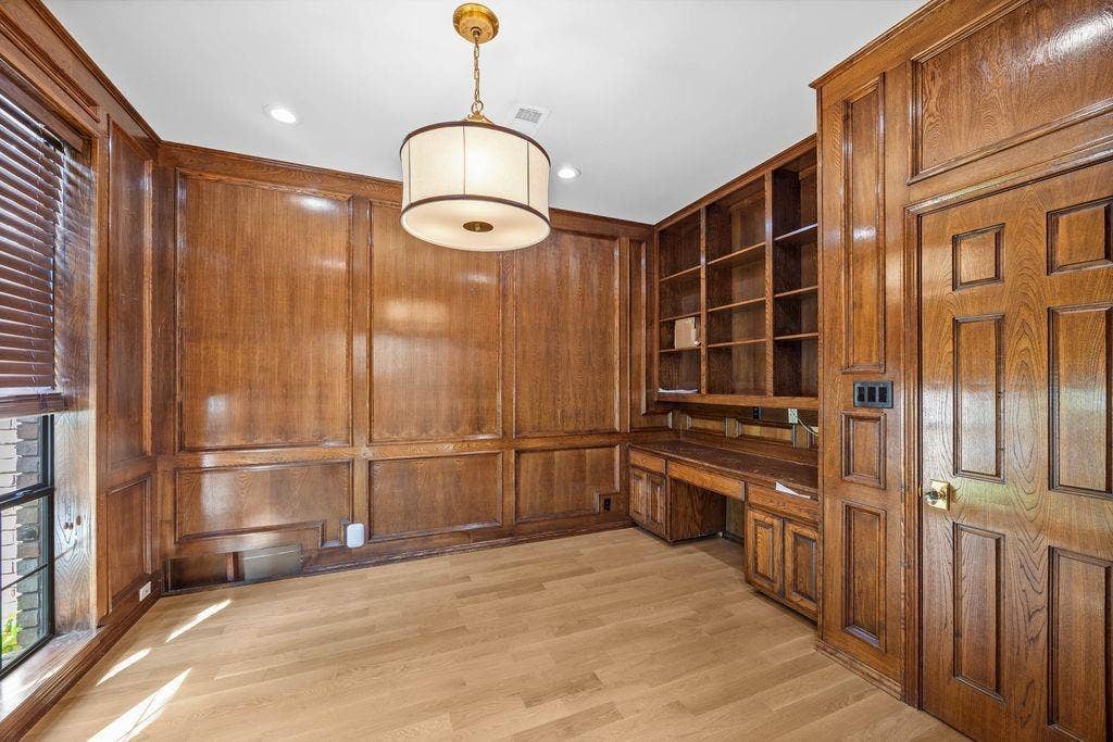 Wood-paneled walls with intricate millwork, built-in floor-to-ceiling cabinetry, integrated desk space, wood-finish flooring, and a drum-style pendant light fixture