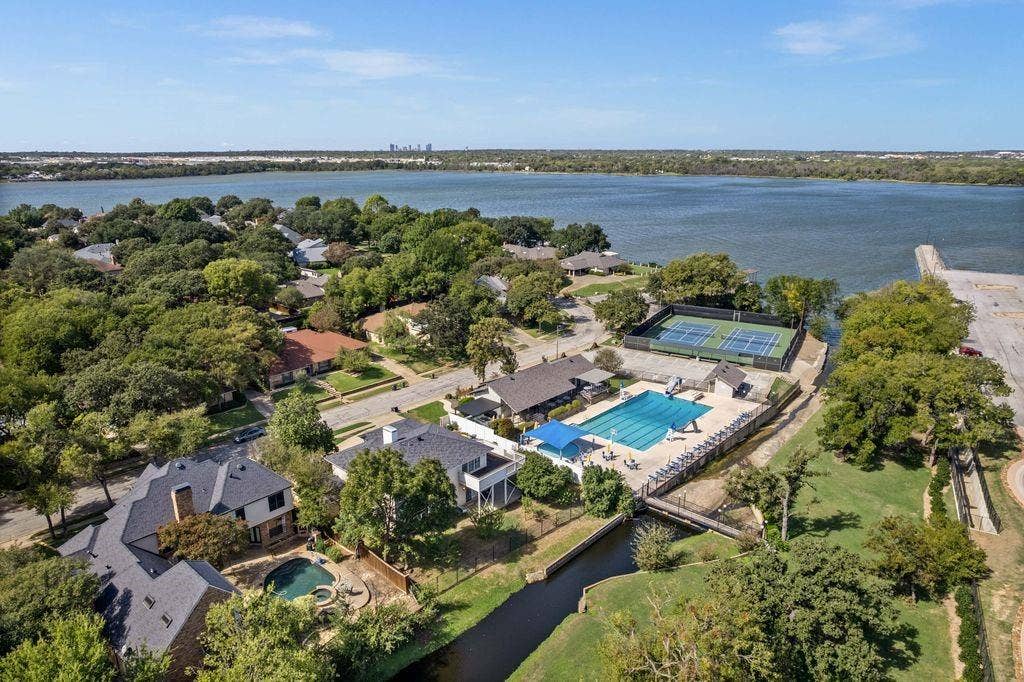 Aerial perspective of a lakeside residential neighborhood featuring extensive shoreline, a swimming pool, and multiple tennis courts