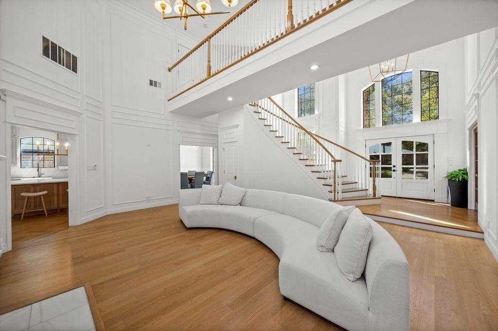 Two-story foyer featuring wood-finish flooring, a sweeping staircase with a wood-accented railing, extensive wall molding, and floor-to-ceiling windows