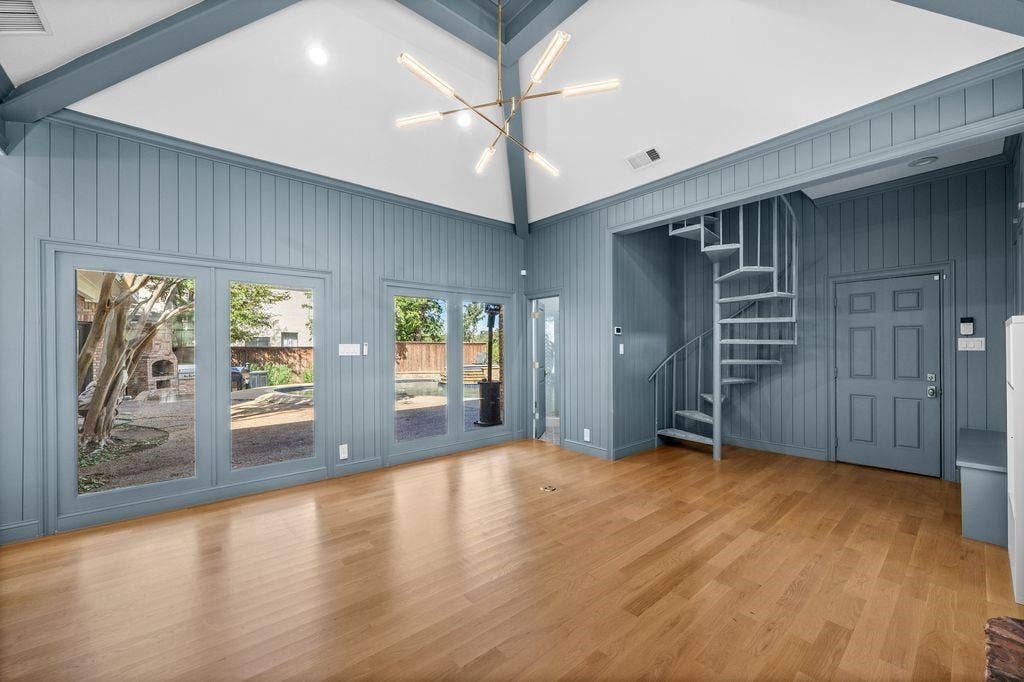 Vaulted ceiling with exposed beams, wood-finish flooring, vertical plank wall paneling, metal spiral staircase, and multi-panel glass doors