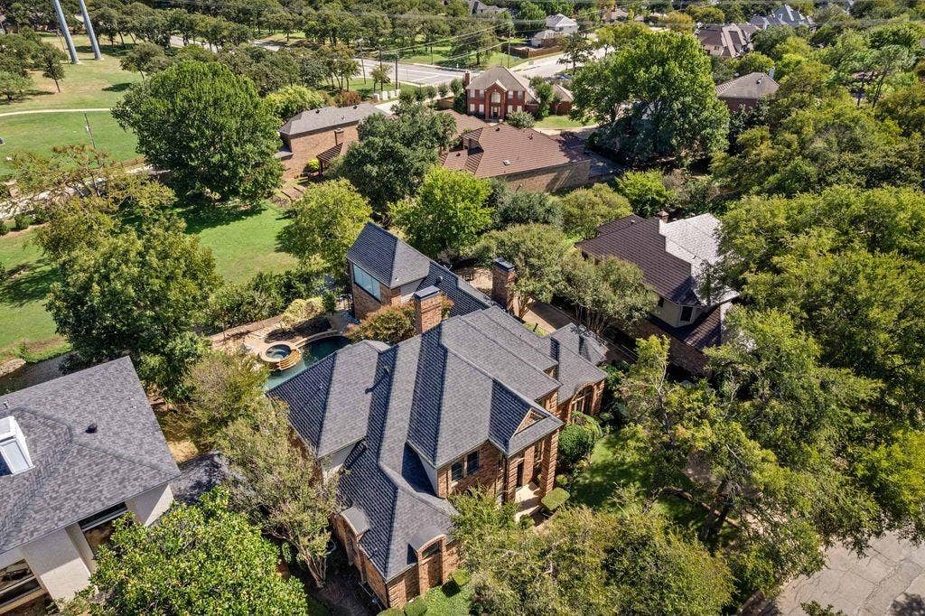 Aerial perspective of a multi-gabled brick residence featuring a multi-level shingle roof, integrated swimming pool with spa, and mature landscaping