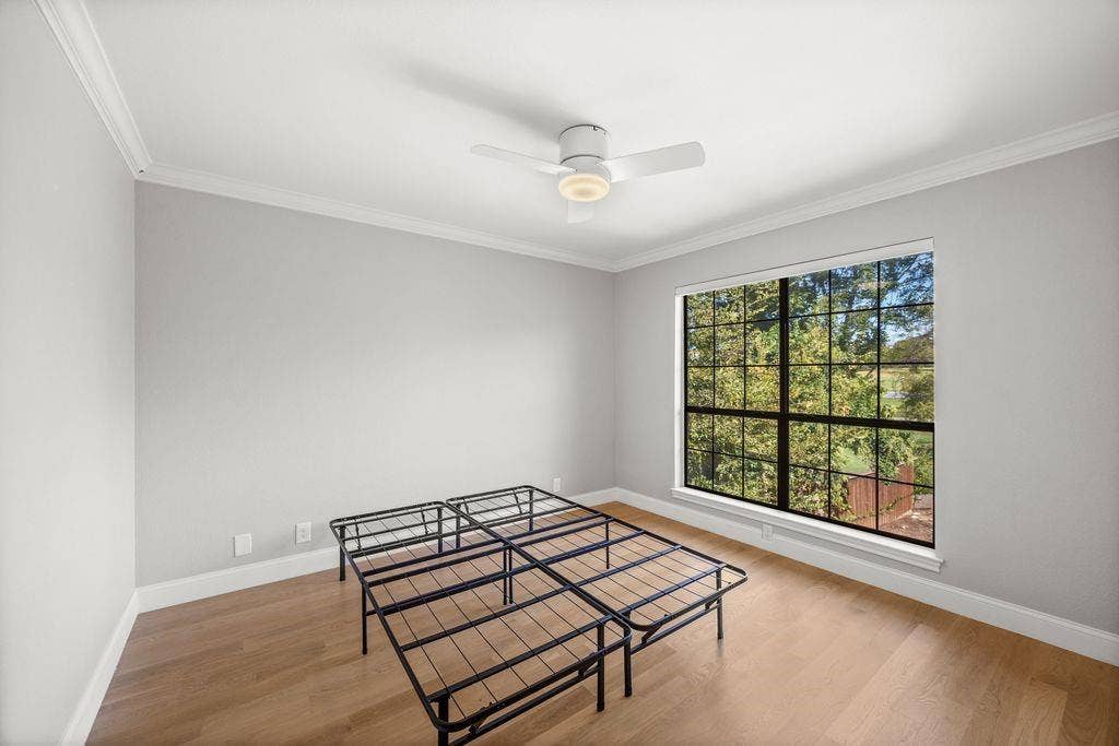 Interior space featuring neutral-toned walls, wood-finish flooring, crown molding, a multi-pane grid window, and a ceiling-mounted light fixture with fan blades