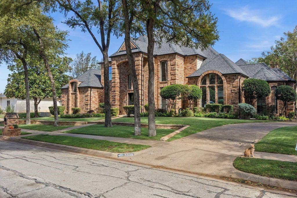 Brick exterior featuring arched windows, a multi-gabled roofline, a columned portico, and mature landscaping