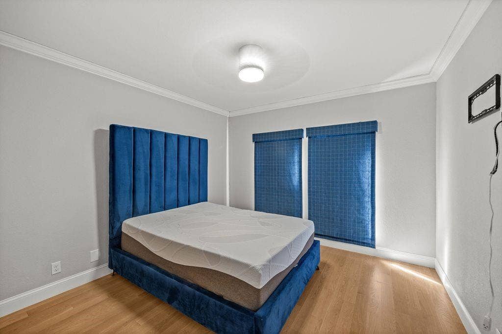 Room featuring wood-finish flooring, crown molding, and two windows with blue grid-patterned roller shades