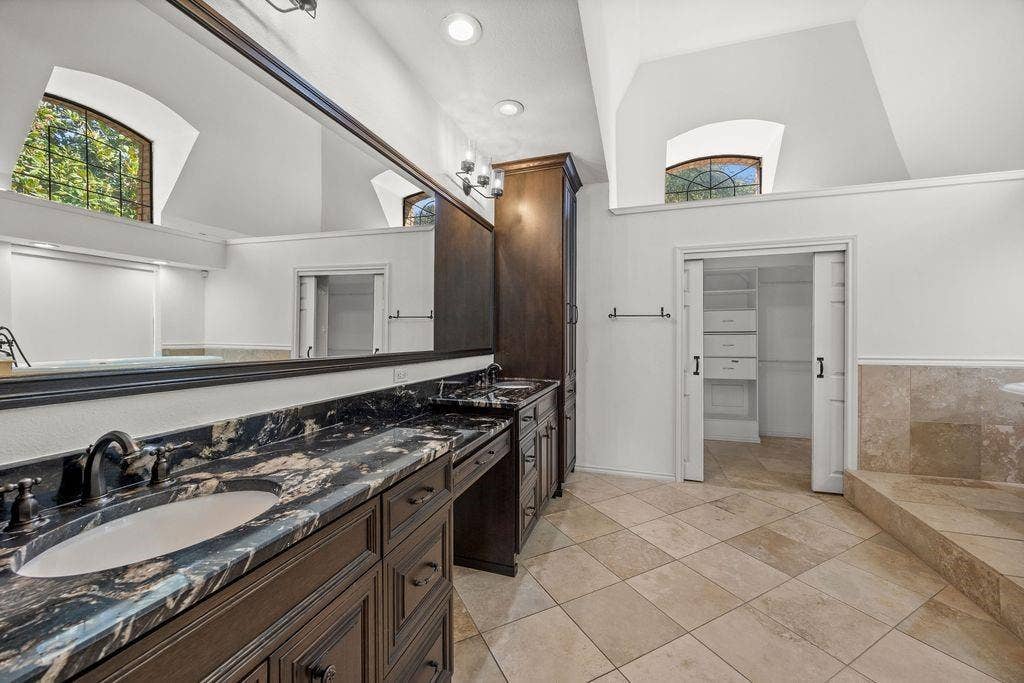 Double vanity featuring dark wood cabinetry, integrated stone countertops with dual undermount sinks, full-width mirror, recessed lighting, and built-in linen storage