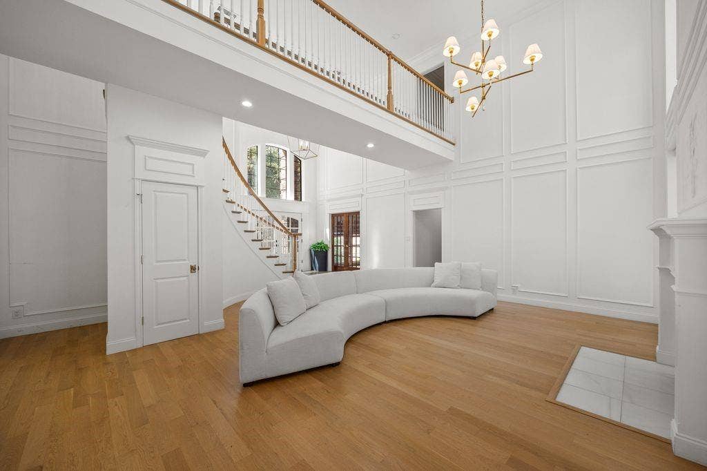 Double-height ceiling, decorative wall paneling, curved staircase with wood railings, wood-finish flooring, and multi-arm chandelier